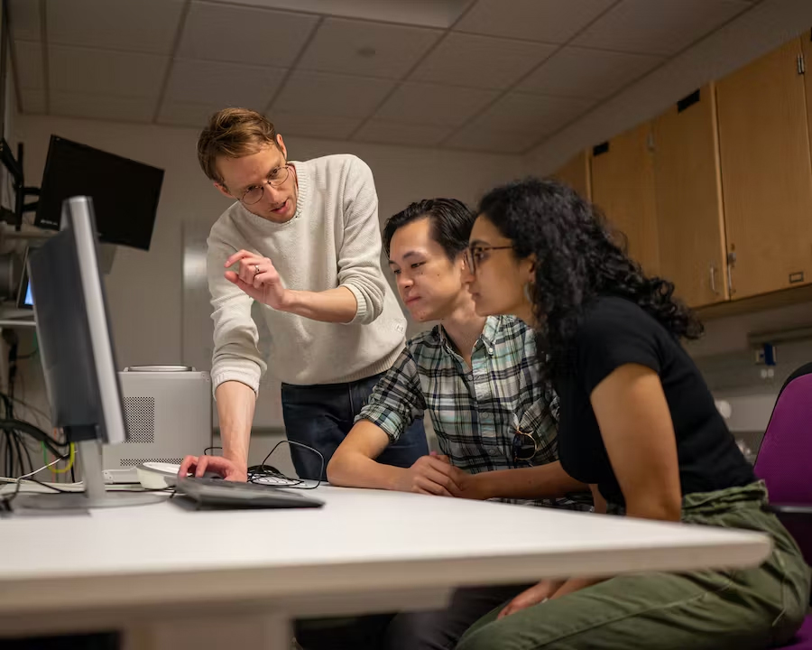 Alex Huth (left), discusses the semantic decoder project with Jerry Tang (center) and Shailee Jain (right) in the biomedical imaging center at The University of Texas at Austin. The researchers trained their semantic decoder on dozens of hours of brain activity data from participants, collected in an fMRI scanner. Photo credit - Nolan Zunk/University of Texas at Austin.