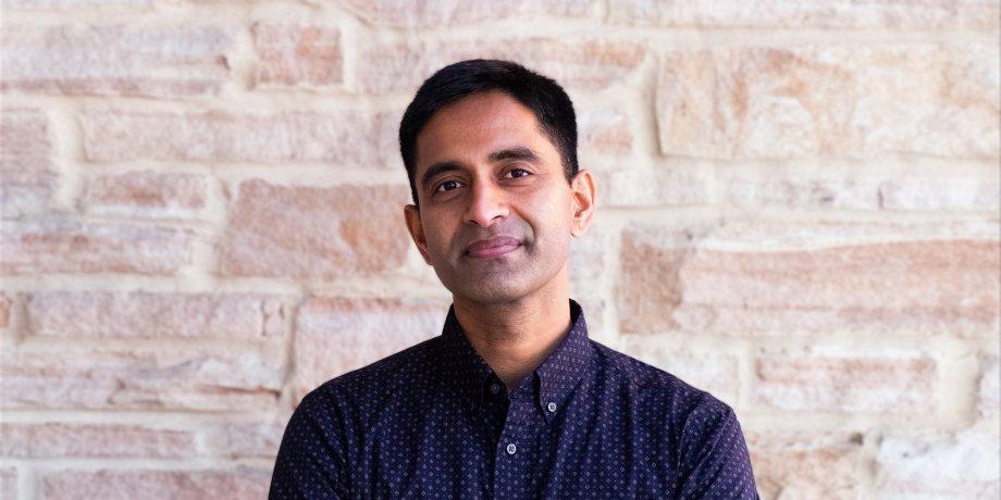 UT Computer Science Professor Aditya Akella in blue button down shirt in front of limestone wall