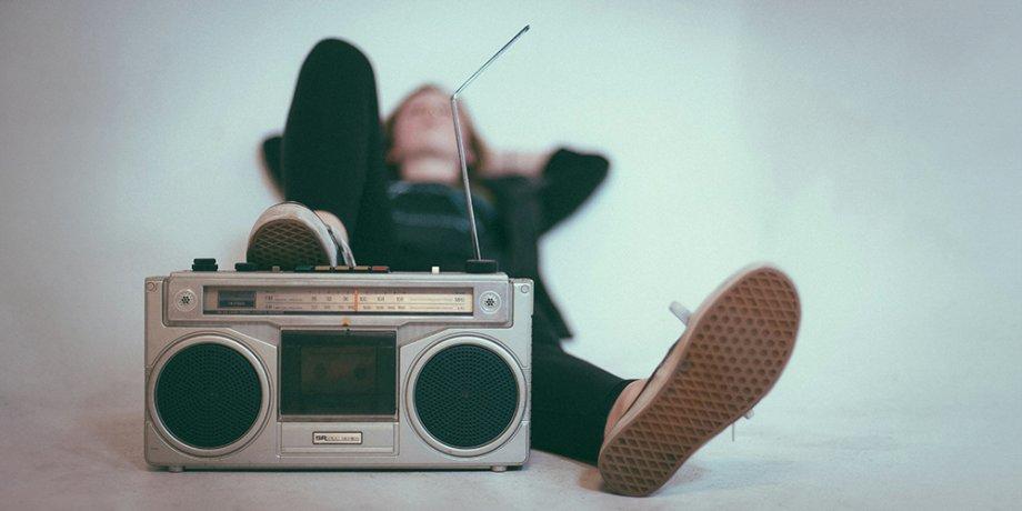 Young person lounging back with a boombox under their right foot listening to music.