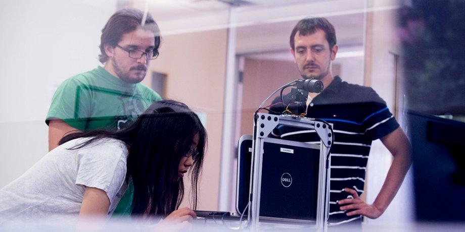 Three students working in a computer science lab together looking at a segway robot.