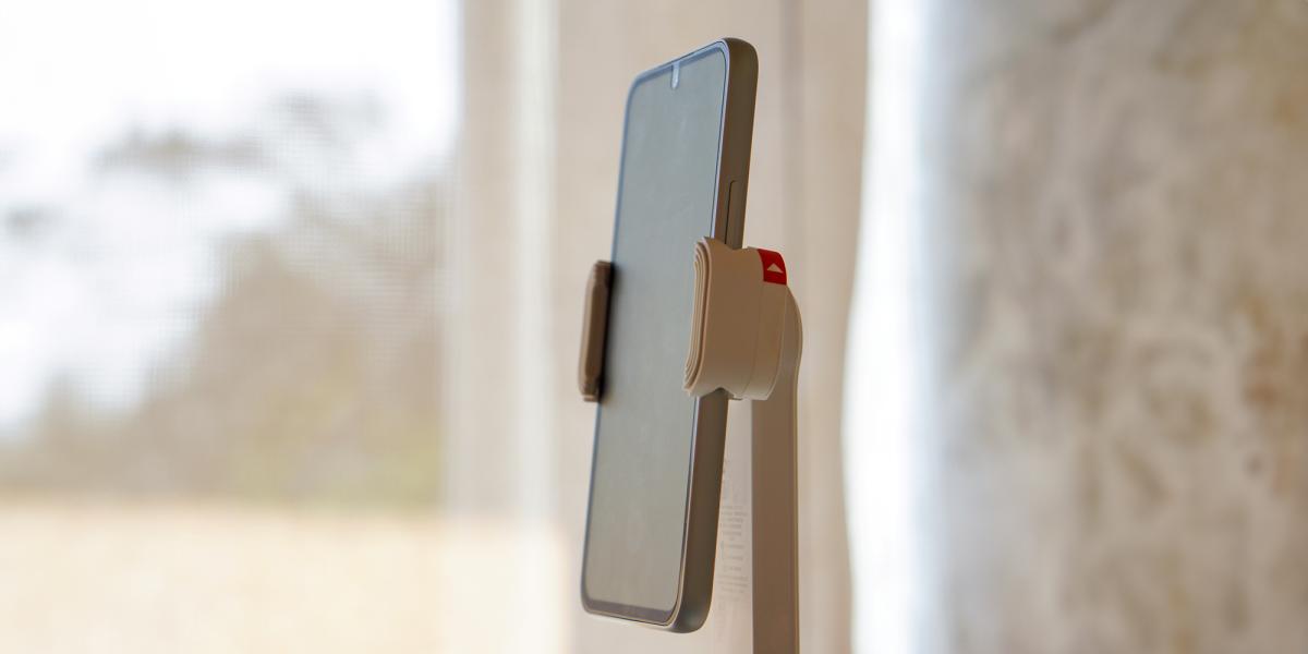 Smart phone positioned on a phone tripod in a netural-tone, naturally lit room with a large window in the background.