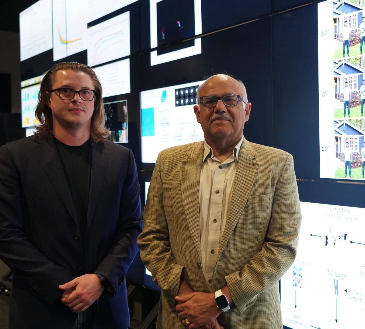 Computer scientists Ryan Farell and Chandrajit Bajaj standing side-by-side in front of the visualization wall in the POB Vis Lab.