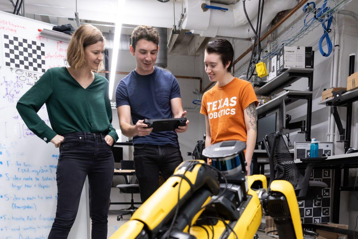 Three people standing in a robotics lab looking at a screen involving robotics.