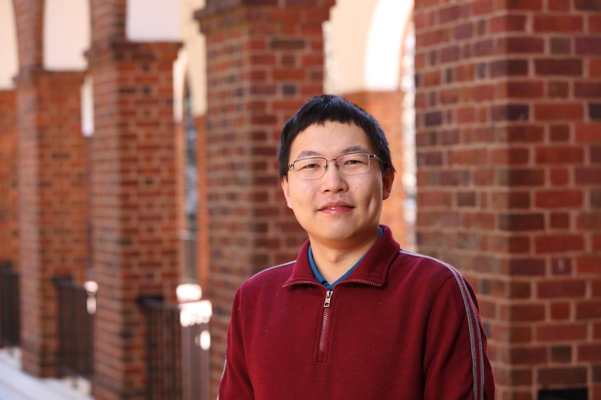 David Wu wearing a read jacket outside with red brick columns in the background.