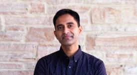 UT Computer Science Professor Aditya Akella in blue button down shirt in front of limestone wall