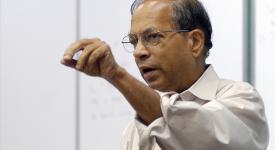 Jayadev Misra teaching class in front of white board and gesturing with his hand.