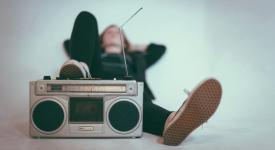 Young person lounging back with a boombox under their right foot listening to music.