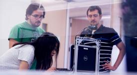 Three students working in a computer science lab together looking at a segway robot.