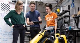 Three people standing in a robotics lab looking at a screen involving robotics.