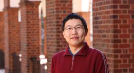 David Wu wearing a read jacket outside with red brick columns in the background.