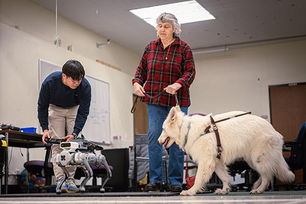 Hochul Hwang working with a robotic guide dog while Gail Gunn works with her guide dog.