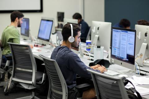 Student working at computer with headphones on in the GDC computer lab.