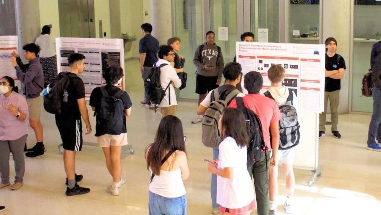 Students gathered in GDC Atrium, looking at student research posters.