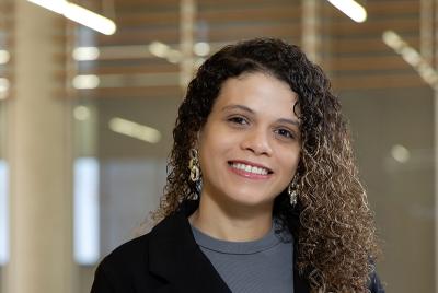 Paula Martinez wearing a grey top with a black blazer, against a blurred background